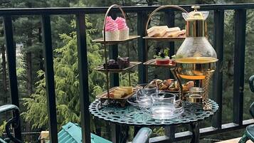 A balcony with a table set for a tea service, surrounded by metal chairs, overlooking a forested area.