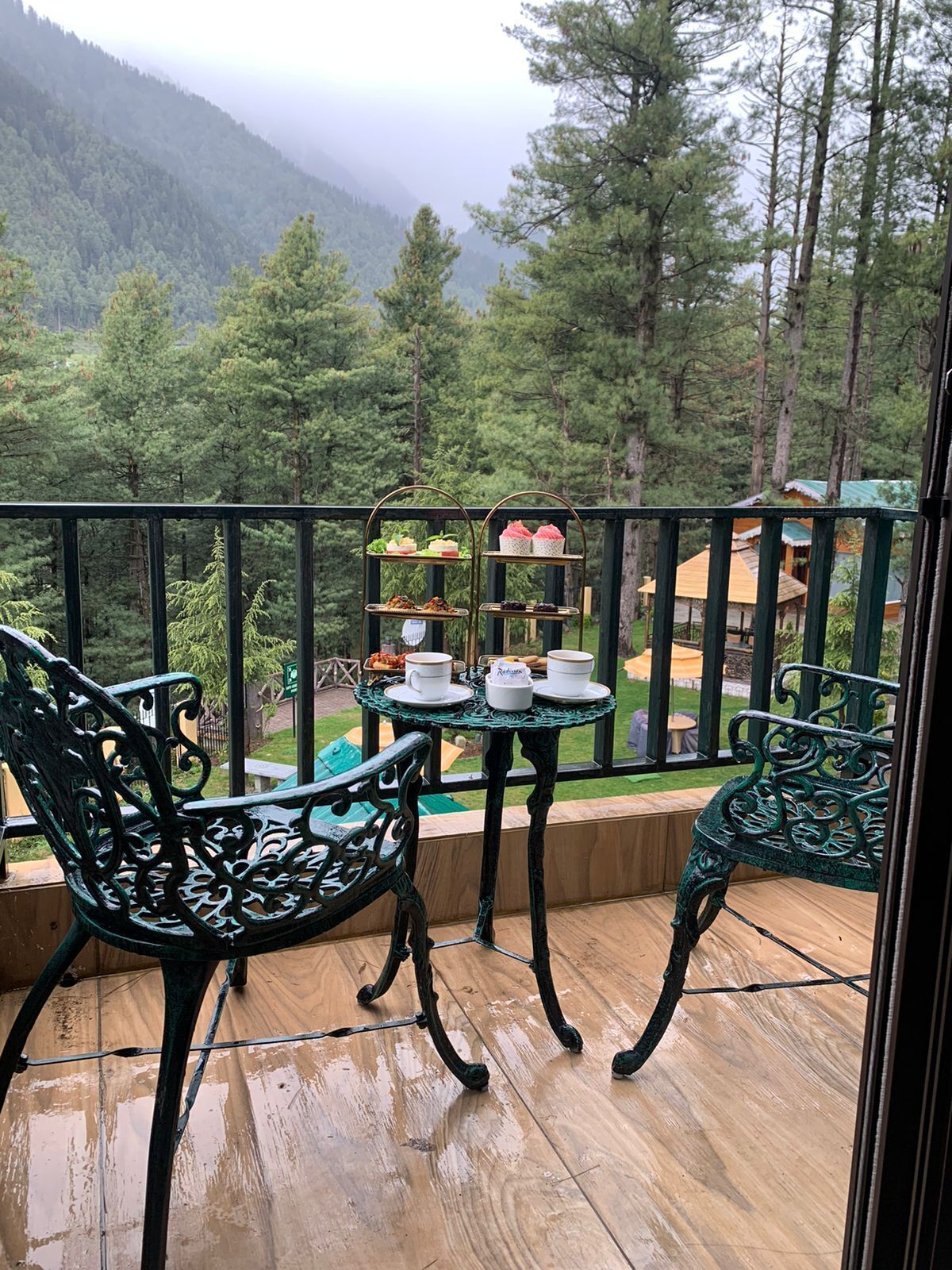 A balcony with two chairs and a small table with a tea set.
