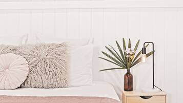 A neatly made bed with fluffy pillows, a bedside table with a vase of flowers and a lamp, and a white wall with vertical paneling.