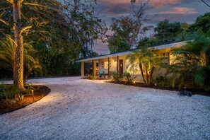 Una casa con vialetto sterrato, circondata da alberi e piante.