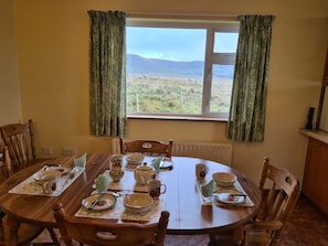 A dining area with a table set for four, chairs, a window with curtains, and a view of the outdoors.