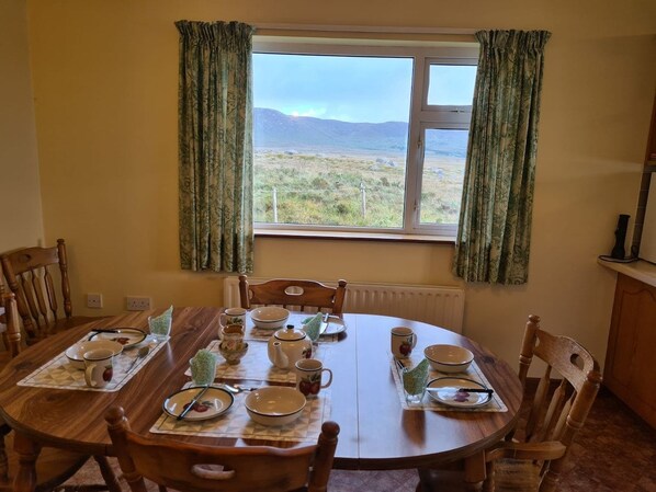 Un comedor con una mesa dispuesta para cuatro personas, sillas, una ventana con cortinas y vistas al exterior.