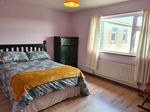 Un dormitorio con cama, cómoda, radiador y ventana con cortinas.