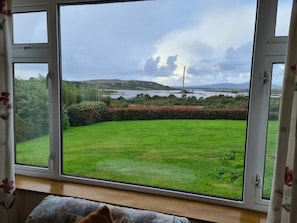 A room with a large window overlooking a well-maintained lawn and distant hills.