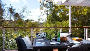 Un espace de restauration en plein air avec une table dressée pour deux personnes, entouré de chaises et de coussins en osier, donnant sur un jardin luxuriant.