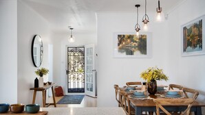 Un coin repas avec une table en bois dressée pour quatre personnes, entourée de chaises en bois. Deux lampes suspendues sont fixées au mur au-dessus de la table.