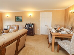 A dining area with a wooden table set for four, a leather sofa, a dark wooden cabinet with drawers, and a white door.