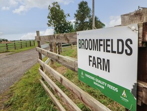 A sign for Broomfields Farm with a wooden fence and grassy field in the background.