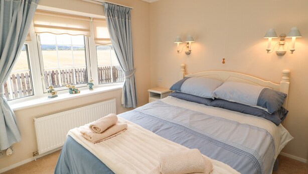 Ein Schlafzimmer mit einem großen Bett, einem Fenster mit Vorhängen, einem Nachttisch und Wandleuchten.