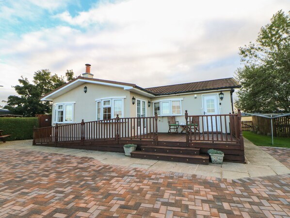 A two-story house with a brick patio, a wooden deck, and a fenced backyard.