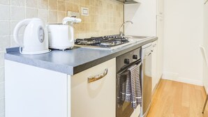 Une petite cuisine équipée d’une cuisinière à gaz, d’une bouilloire et d’un grille-pain posés sur le plan de travail.