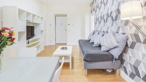 Un salon moderne avec un canapé gris, un meuble TV blanc et un mur orné d’un motif.