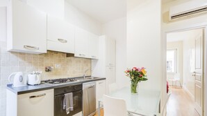 Une cuisine moderne avec des meubles blancs, une cuisinière à gaz, un lave-vaisselle et une table à manger en verre, accompagnée de chaises.