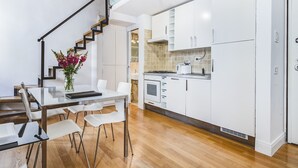 A modern kitchen with white cabinets, a wooden staircase, and a dining area with a glass table and chairs.