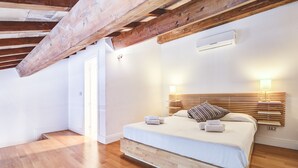 A bedroom with a wooden ceiling, a bed with a headboard, bedside lamps, and a wooden floor.
