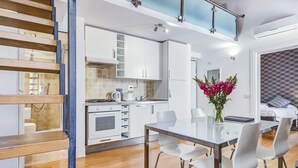 A modern kitchen with white cabinets, a dining table with chairs, and a staircase with wooden steps.