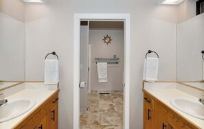 Casa de banho com duas pias, armários de madeira, um espelho e um porta-toalhas.