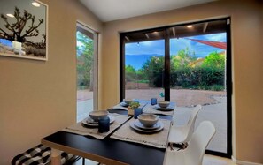 A dining area with a table set for four, a chair, and a view of a garden through large windows.