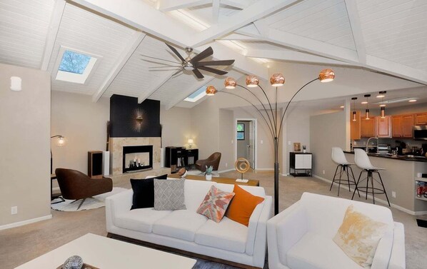 A spacious living area with a high ceiling, a fireplace, and a modern kitchen in the background.