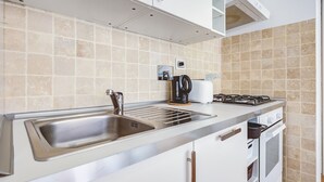 Cuina moderna amb un rentaplat de superfície inoxidable, una cuina a gas i un forn integrat.