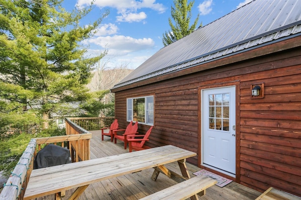 Uma cabana de madeira com varanda, duas cadeiras Adirondack vermelhas e uma mesa de piquenique.