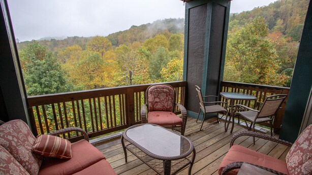 A wooden deck with wicker furniture and a glass table, overlooking a forested area. - Peaceful Blue Ridge Getaway at Echota (Boone)
