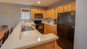 A kitchen with wooden cabinets, a stainless steel sink, a black refrigerator, and a microwave. - Peaceful Blue Ridge Getaway at Echota (Boone)
