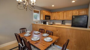 A kitchen with wooden cabinets, a black refrigerator, a microwave, and a dining table set with plates. - Peaceful Blue Ridge Getaway at Echota (Boone)