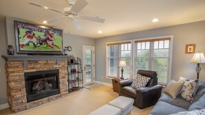A living room with a stone fireplace, a television mounted above it, a leather sofa, a coffee table, and a ceiling fan. - Peaceful Blue Ridge Getaway at Echota (Boone)