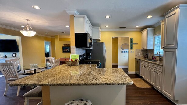 A kitchen with a central island, wooden chairs, and a dining table. - Heated Pool! 2 Master Suites- 5 miles to Clearwater Beach! (Clearwater)