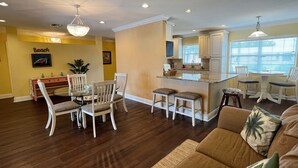 A spacious living room with a large brown sofa, a dining area with a glass table, and a kitchen with white cabinets and a central island. - Heated Pool! 2 Master Suites- 5 miles to Clearwater Beach! (Clearwater)