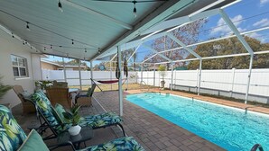 A covered outdoor area with a pool, lounge chairs, and a dining table. - Heated Pool! 2 Master Suites- 5 miles to Clearwater Beach! (Clearwater)