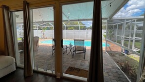 A room with a sliding glass door leading to a patio with a pool, outdoor furniture, and a covered area. - Heated Pool! 2 Master Suites- 5 miles to Clearwater Beach! (Clearwater)
