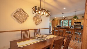 Uma sala de jantar com mesa e cadeiras de madeira, um objeto decorativo no centro e um lustre.