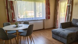 A dining area with a round table and four chairs, a grey sofa, and a window with curtains. - Ideal for mountain lovers, couples and small families  (6653 Bach)