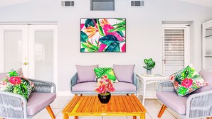 Una sala de estar con dos sofás de mimbre gris, una mesa de centro de madera y un cuadro vibrante con motivos tropicales en la pared.