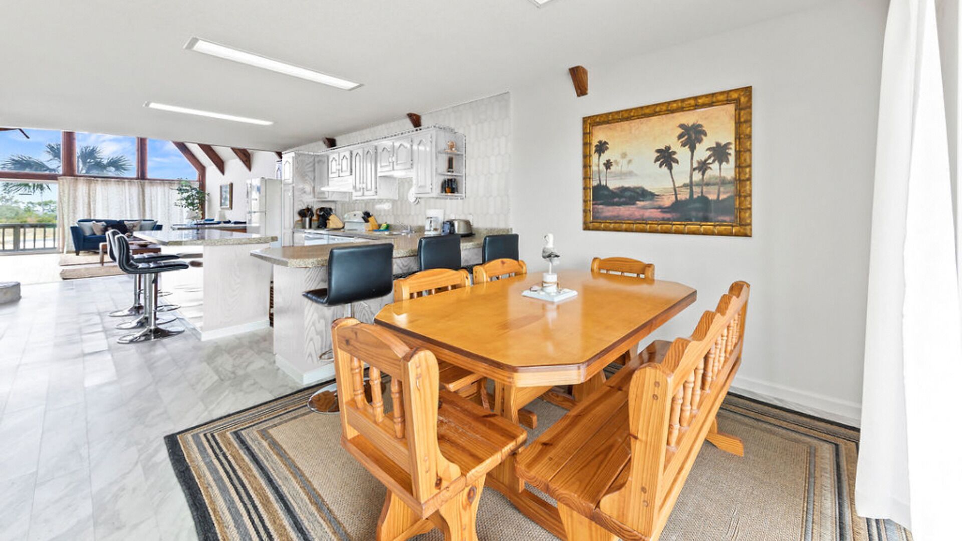 Une cuisine spacieuse équipée d’appareils modernes, un coin repas avec des chaises en bois et une grande fenêtre donnant sur un balcon.