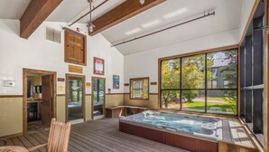 Un jacuzzi en una habitación con pisos de madera, un ventanal con vista a árboles y una puerta que da a una zona de cocina.