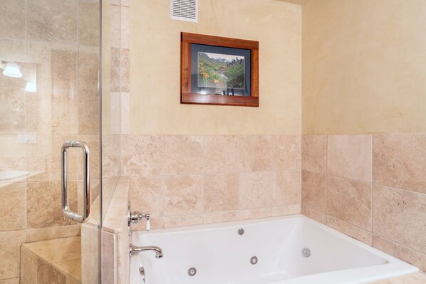 A bathroom with a white bathtub, beige tiles, a framed picture on the wall, and a handrail.