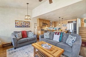 A modern living room with two grey sofas, a wooden coffee table, and a kitchen in the background.