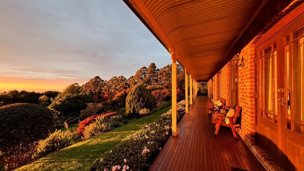 Un espace extérieur abrité, doté d’une terrasse en bois, de murs en briques et offrant une vue sur un jardin aménagé avec différents arbres et arbustes.
