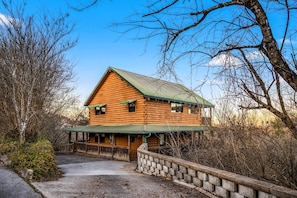 A log cabin with a green roof, a porch, and a stone wall. - Summer Break • Theater • Hot Tub • Games • Pets Ok (Sevierville)