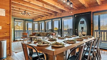 A wooden interior with a dining table set for a meal, large windows, and a cozy seating area.
