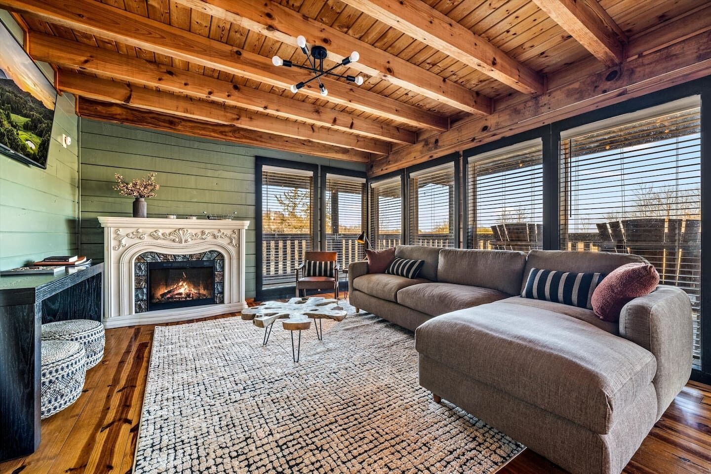 A cozy living room with a fireplace, wooden ceiling, and large windows.