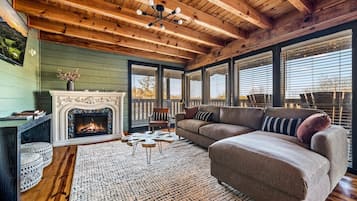 A cozy living room with a fireplace, wooden ceiling, and large windows.