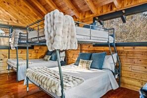 A cabin interior with bunk beds, wooden walls, and a window overlooking trees. - Summer Break • Theater • Hot Tub • Games • Pets Ok (Sevierville)