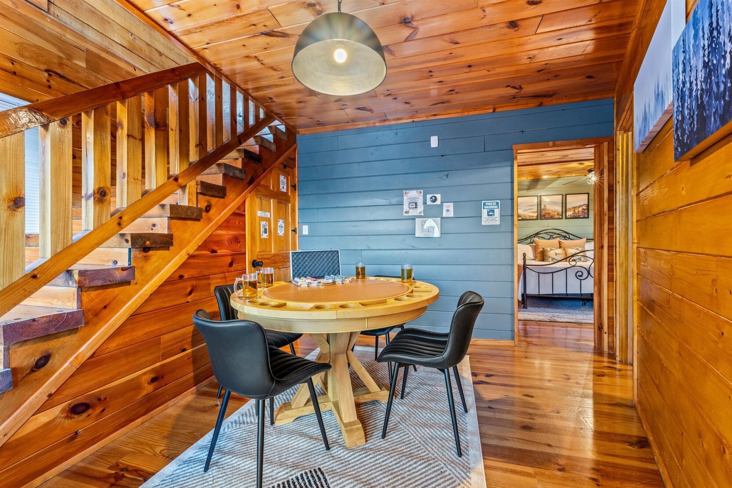 A wooden interior with a round wooden table and four chairs, a staircase, and a bed with a metal frame.