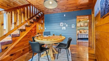 A wooden interior with a round wooden table and four chairs, a staircase, and a bed with a metal frame.