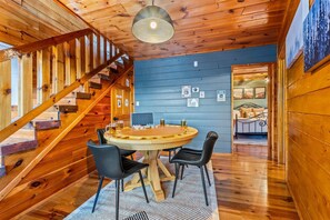 A wooden interior with a round wooden table and four chairs, a staircase, and a bed with a metal frame. - Summer Break • Theater • Hot Tub • Games • Pets Ok (Sevierville)