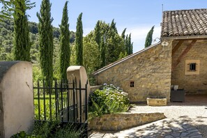 A stone building with a tiled roof, a stone wall, and a gravel courtyard.